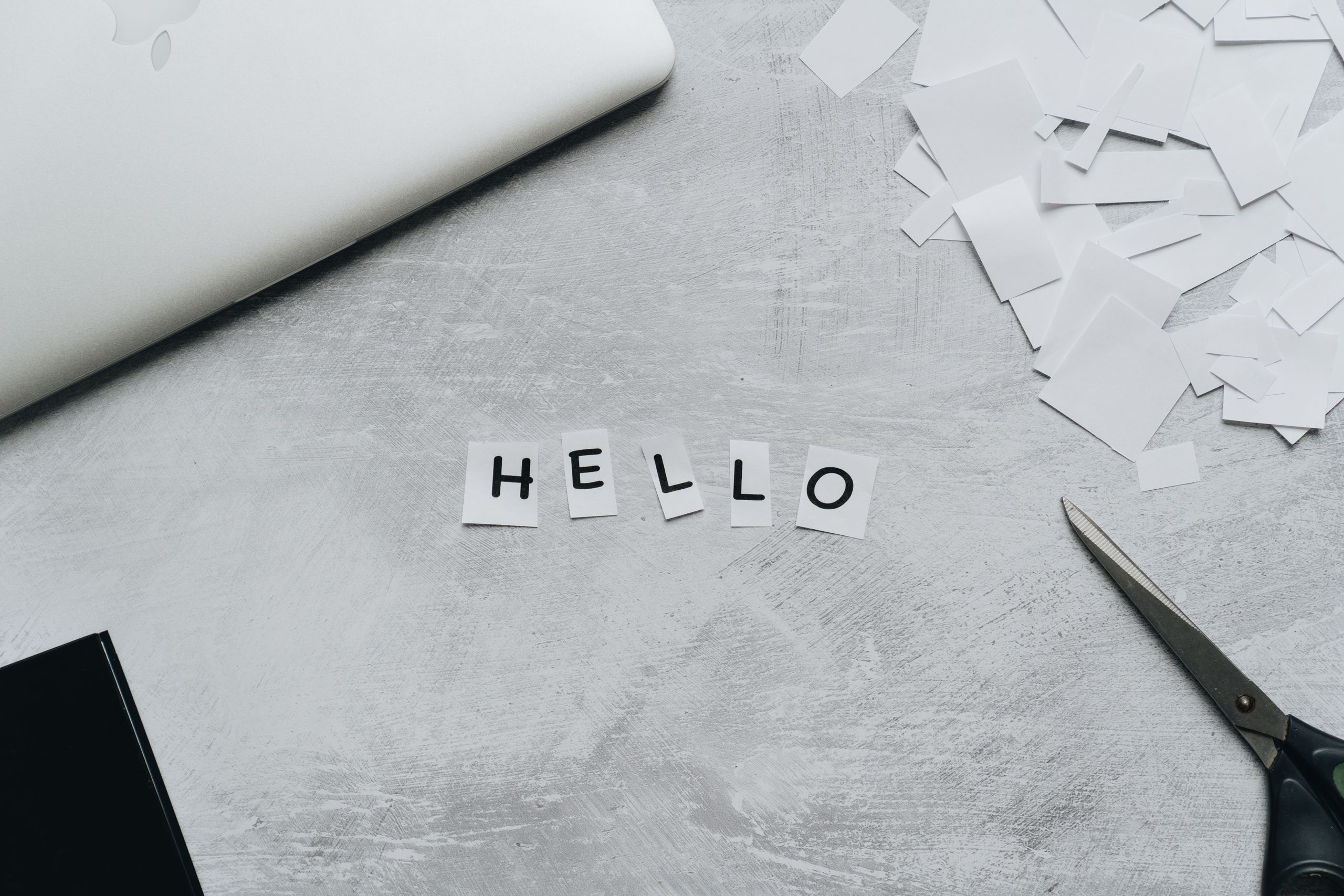Flat lay of a creative workspace with scissors and cut out letters spelling 'hello' on a textured surface.